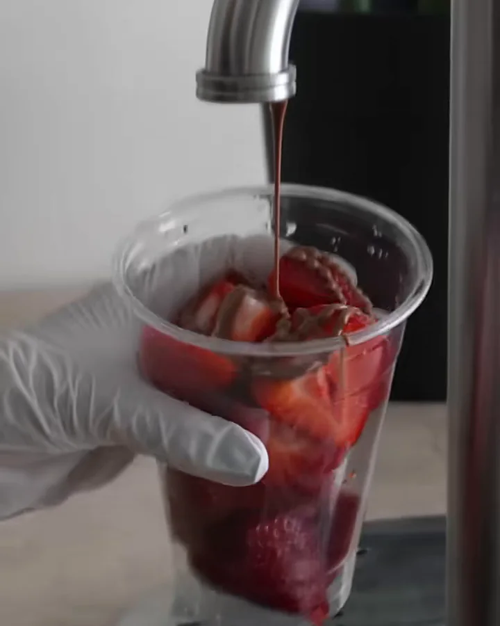Schokolade läuft aus dem Hahn über frische Erdbeeren im RIO-Becher